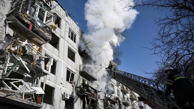 رجال إطفاء يعملون في مبنى تعرض للقصف في بلدة تشوغويف شرقي أوكرانيا - 24 شباط (AFP)