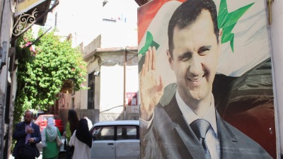 أشخاص يسيرون بالقرب من صورة لرئيس النظام السوري بشار الأسد في دمشق - 19 أيار 2023 (رويترز)